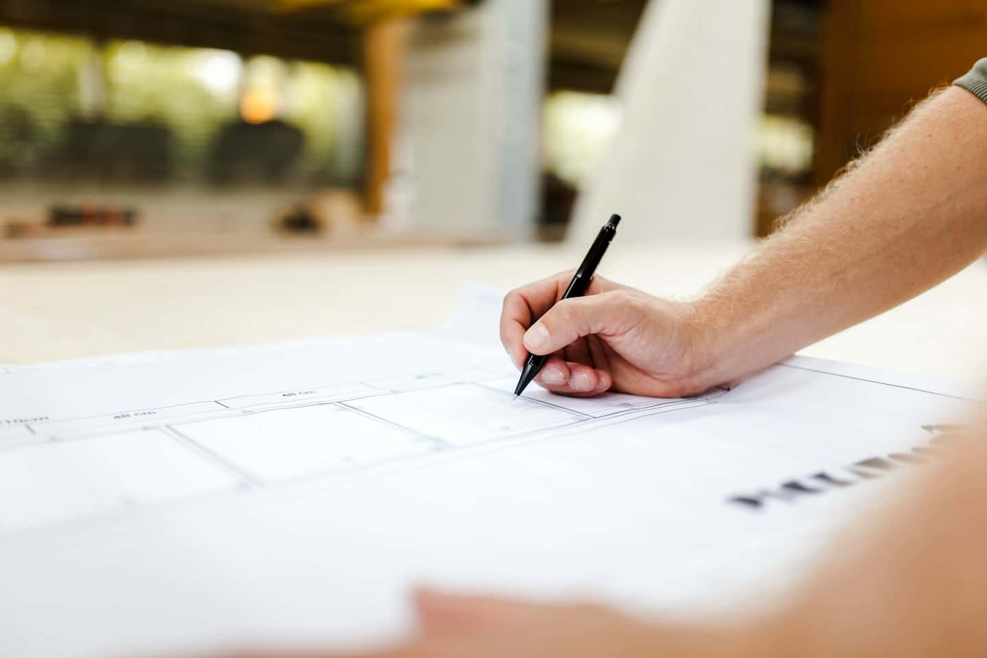 Hand holding a pen and drawing on architectural blueprints.