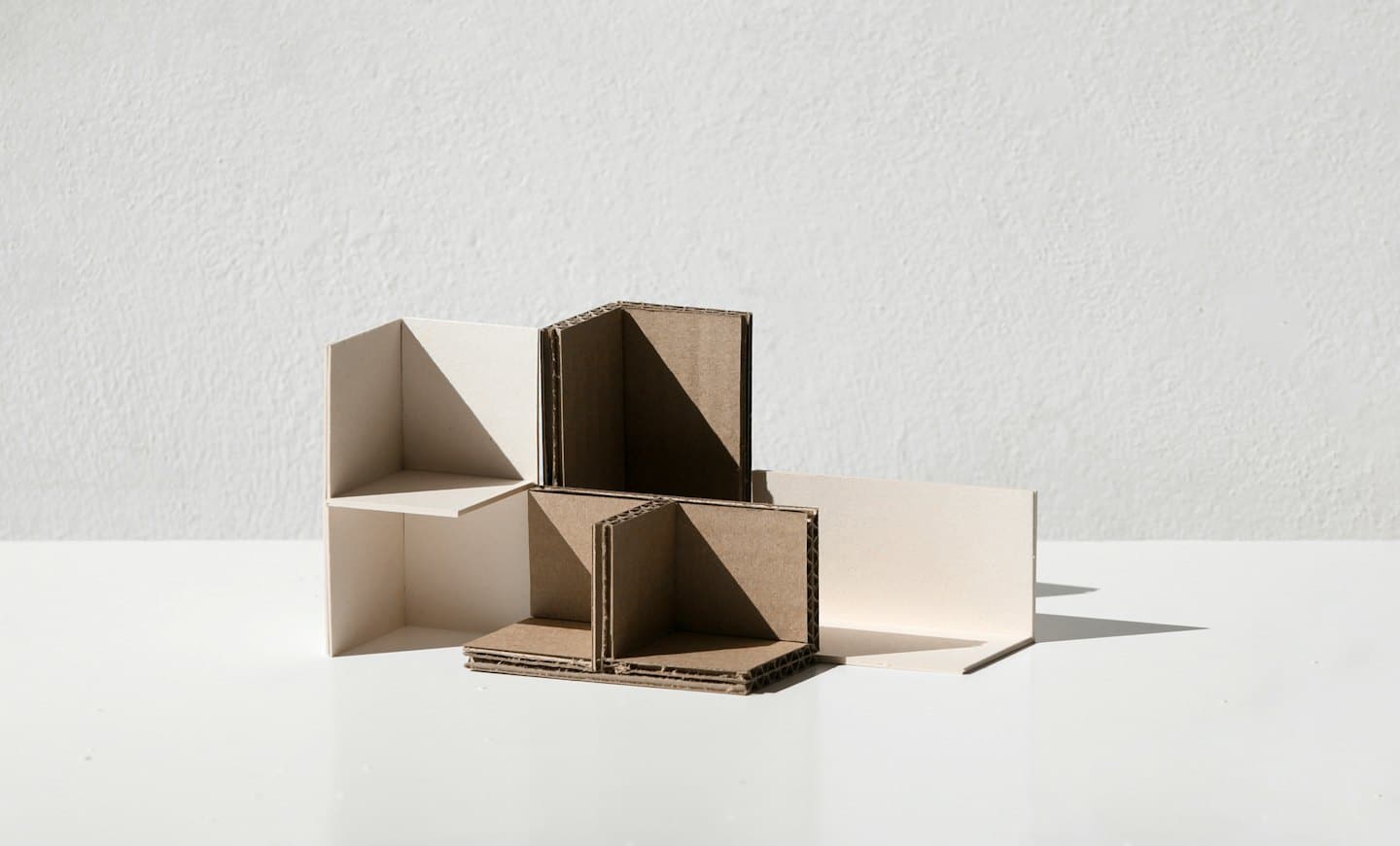 Abstract architectural models made of paper sit on a white table.